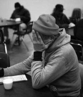 senior in a homeless shelter at dinner covering face with hand